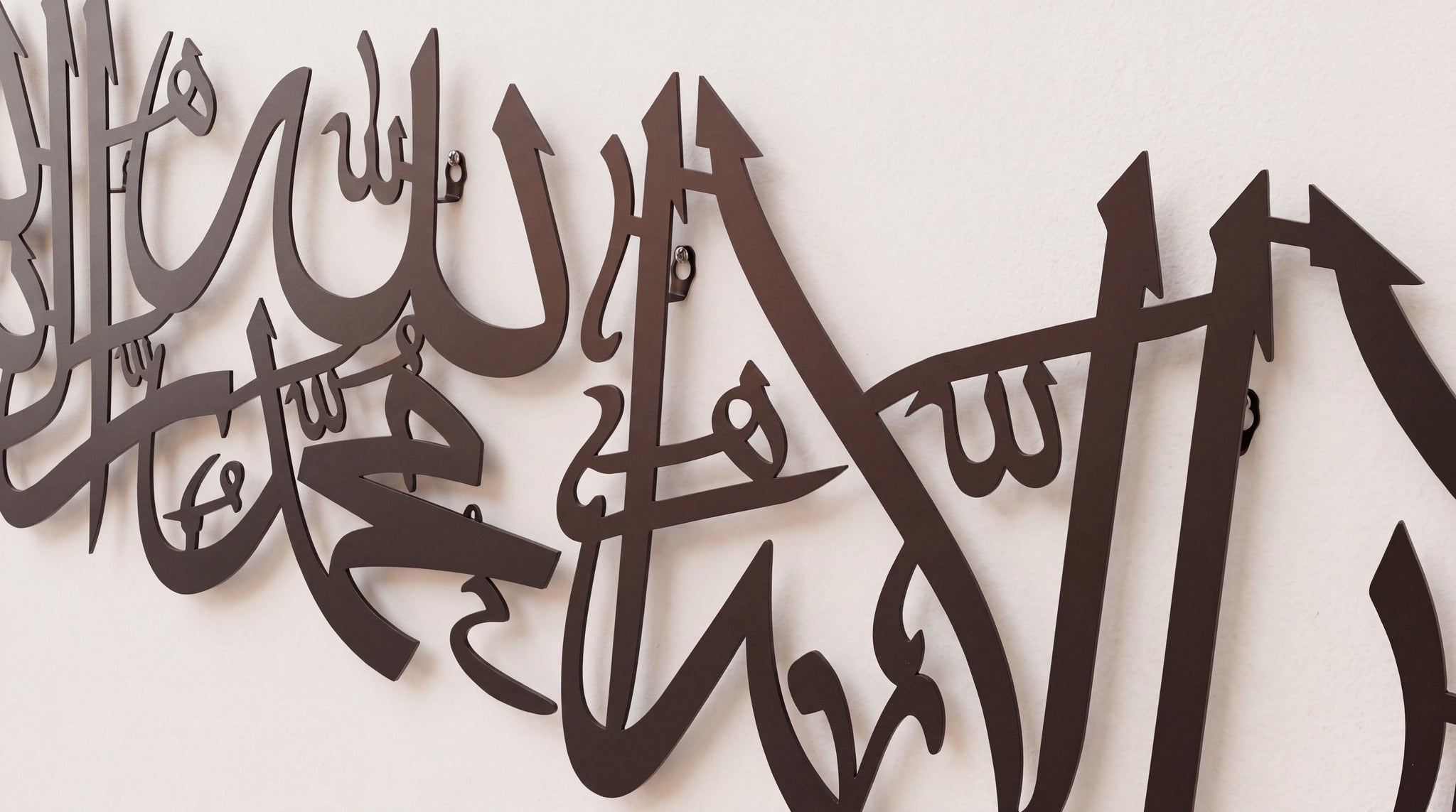 Shahada Kalima Black metal Islamic wall art featuring Arabic calligraphy of 'Allah' mounted on a plain off-white wall.