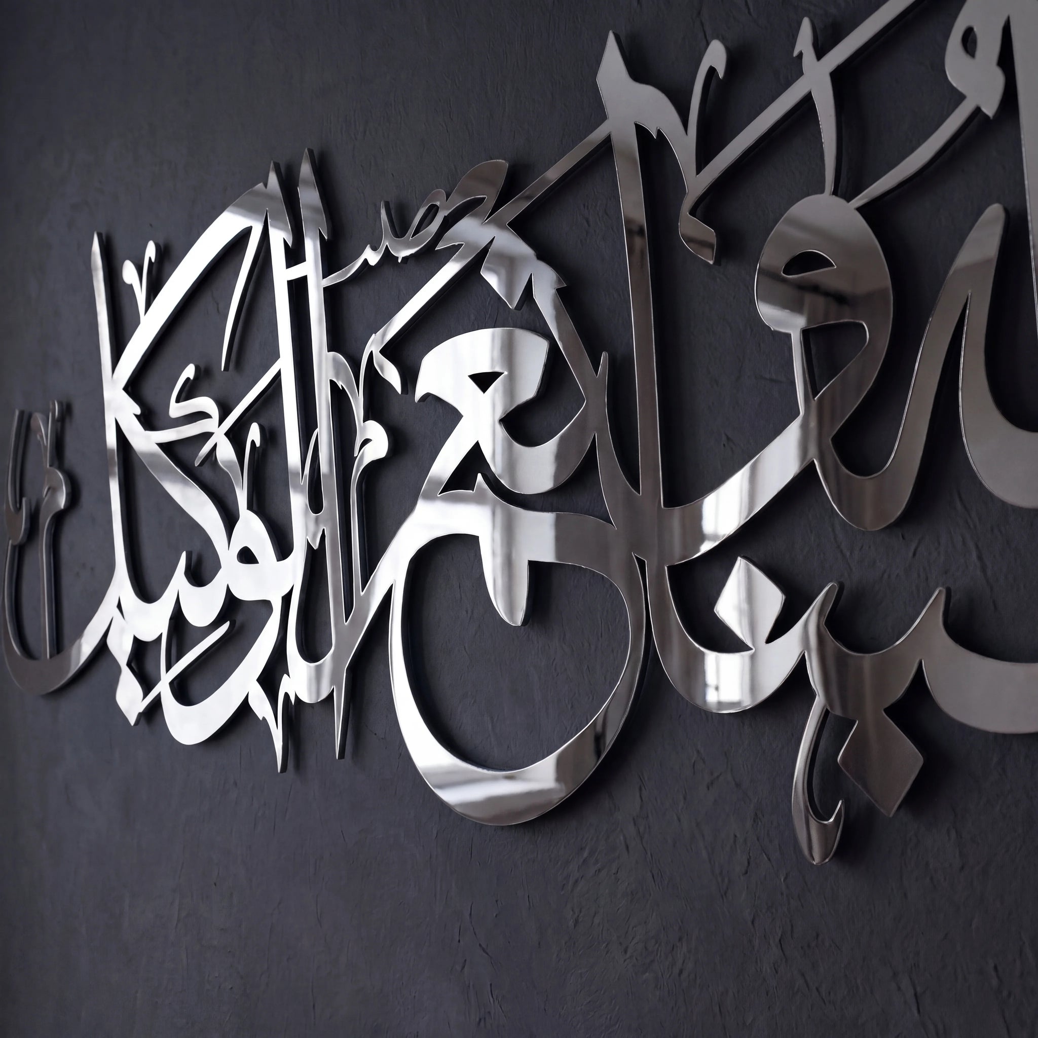 Chrome silver metallic Arabic calligraphy wall art mounted on a dark textured wall.