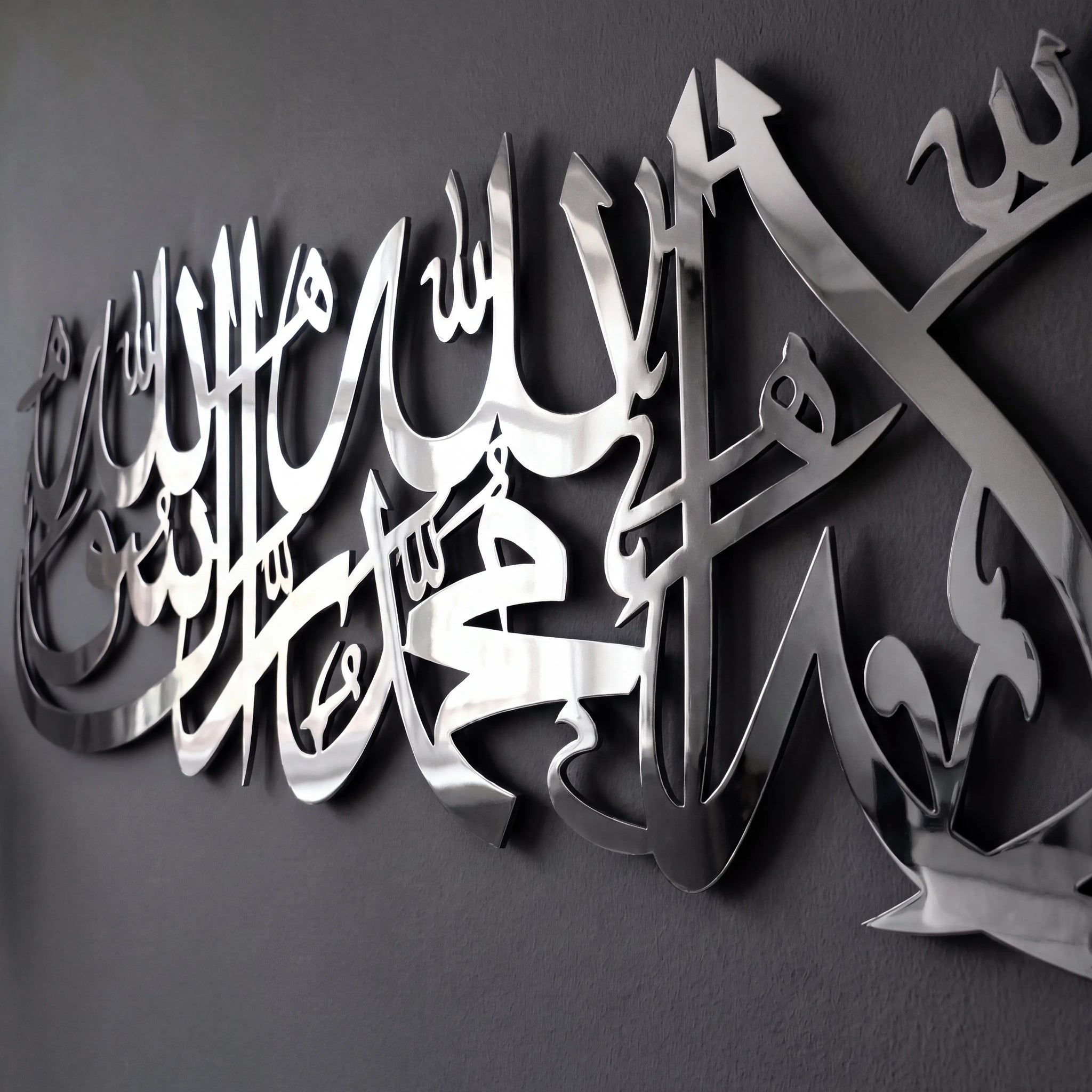 Shiny Stainless Steel metallic Arabic calligraphy wall art mounted on a dark gray wall.