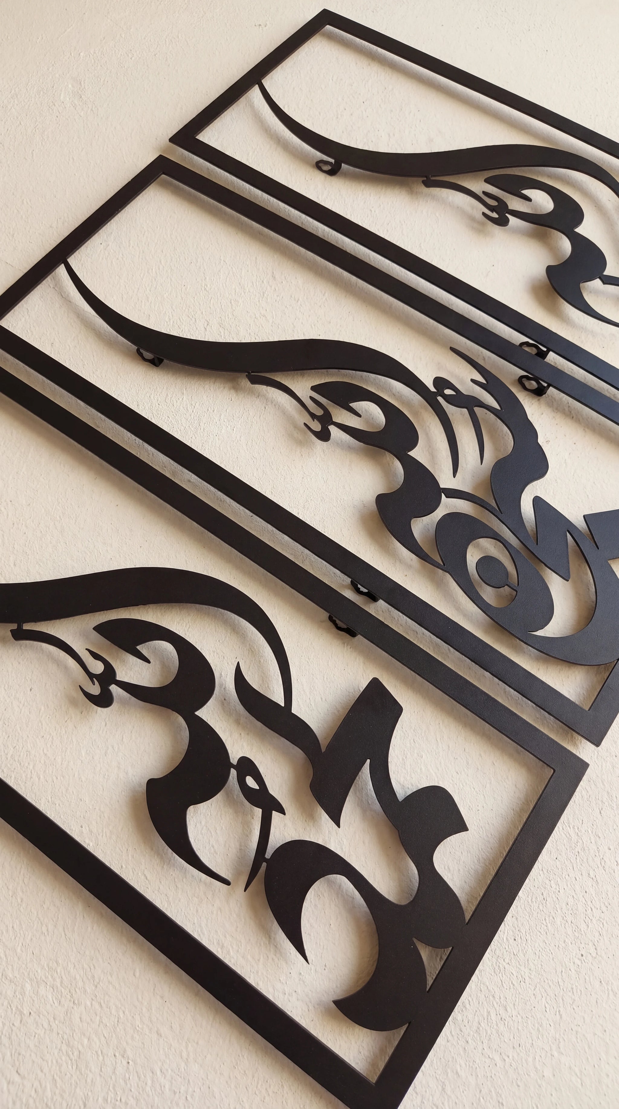 Three black metal wall art panels with stylized abstract cutout designs, arranged diagonally on a light beige textured wall.