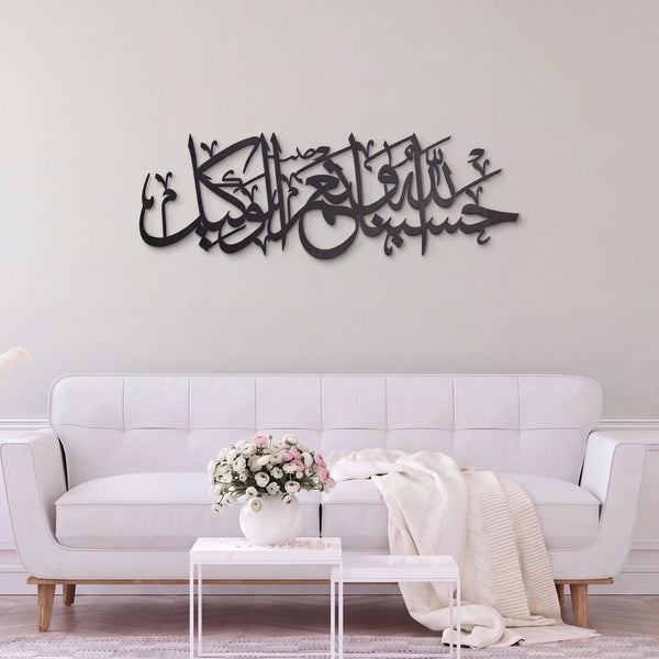 Black metallic Arabic calligraphy wall art mounted on a light gray wall above a modern white sofa in a styled living room.
