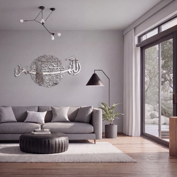 A modern living room with a gray sofa, round black ottoman, white rug, and a large Darood Shareef Arabic calligraphy Chrome Silver wall art piece mounted on the gray wall above the sofa.