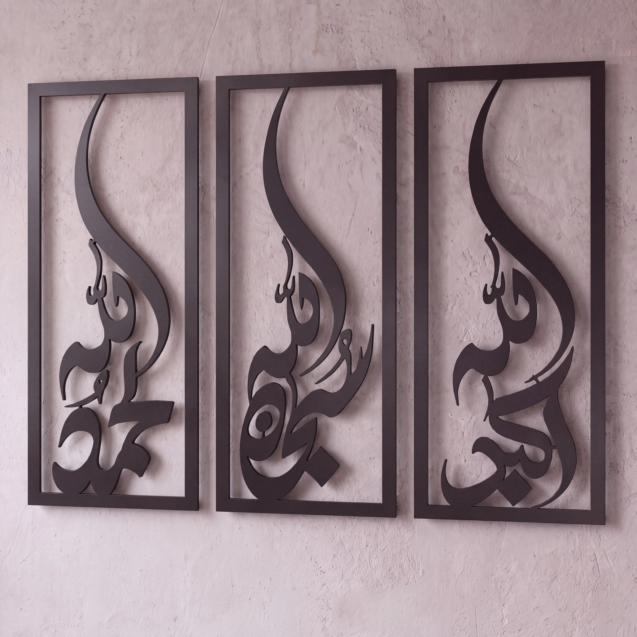 Three-piece black metal Islamic wall art set featuring stylized Arabic calligraphy of the letter 'Subhanallah Alhamdulillah Allah Ho Akbar' in a vertical rectangular frame, mounted on a textured light beige plaster wall.