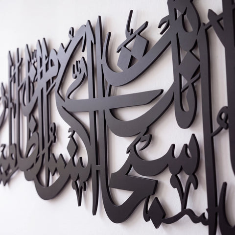Black metal Islamic wall art featuring elegant Arabic calligraphy, shown mounted on a plain white wall.