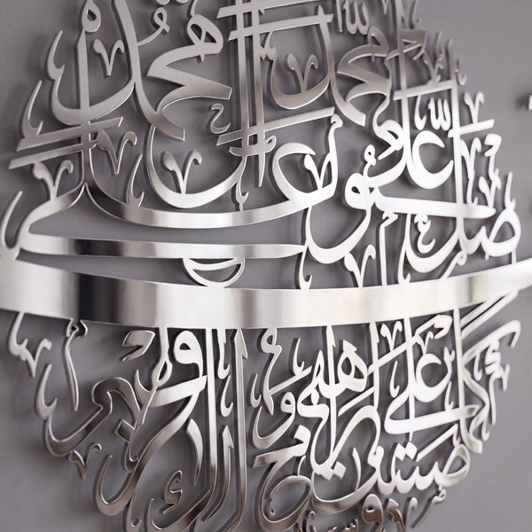 Silver metal Islamic wall art featuring intricate Arabic calligraphy, shown mounted on a gray wall.