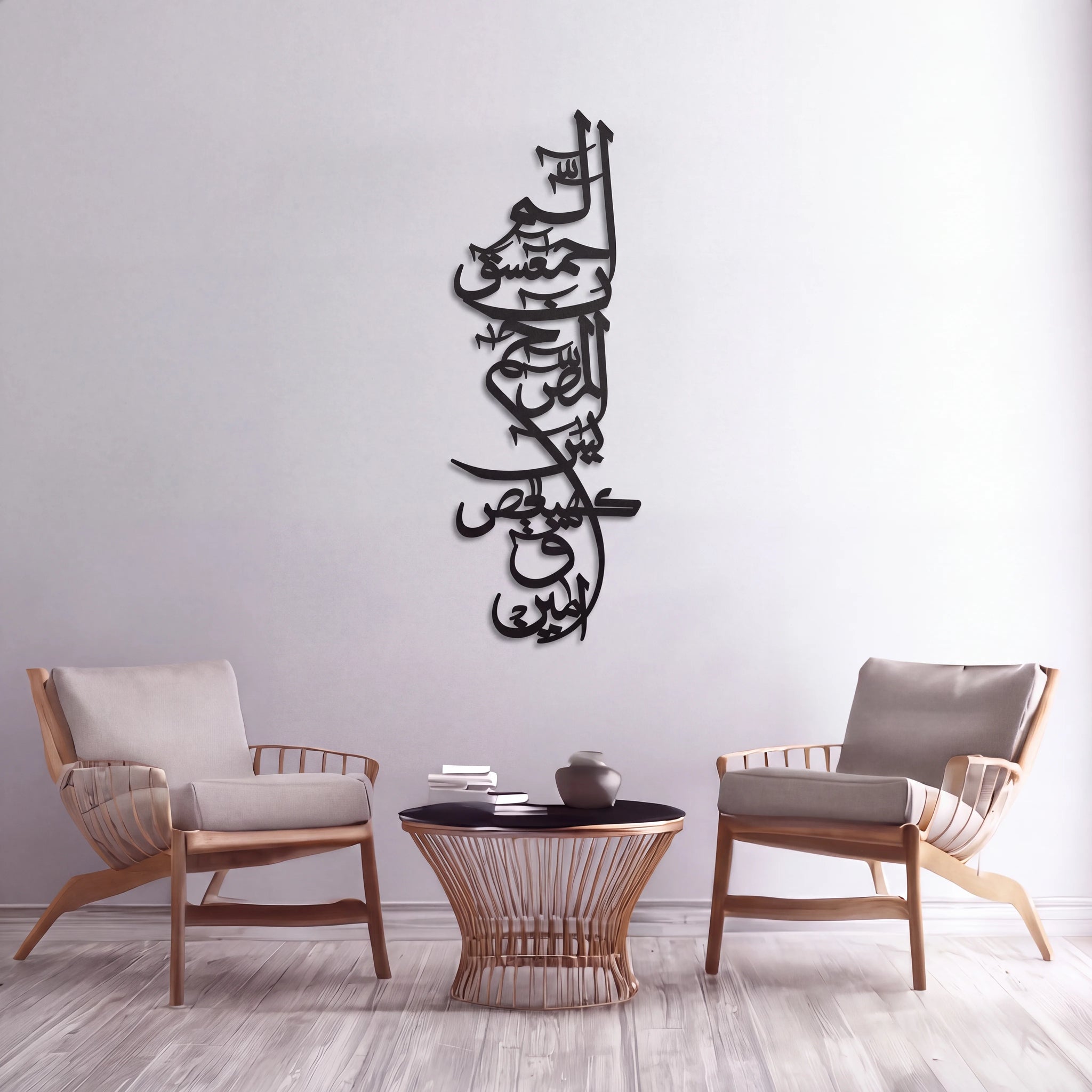 Black Lohe Qurani metal Arabic calligraphy wall art mounted on a light gray wall above a small round table, with two wooden armchairs on either side in a styled interior setting.