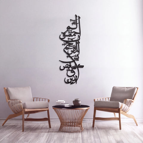 Black Lohe Qurani metal Arabic calligraphy wall art mounted on a light gray wall above a small round table, with two wooden armchairs on either side in a styled interior setting.