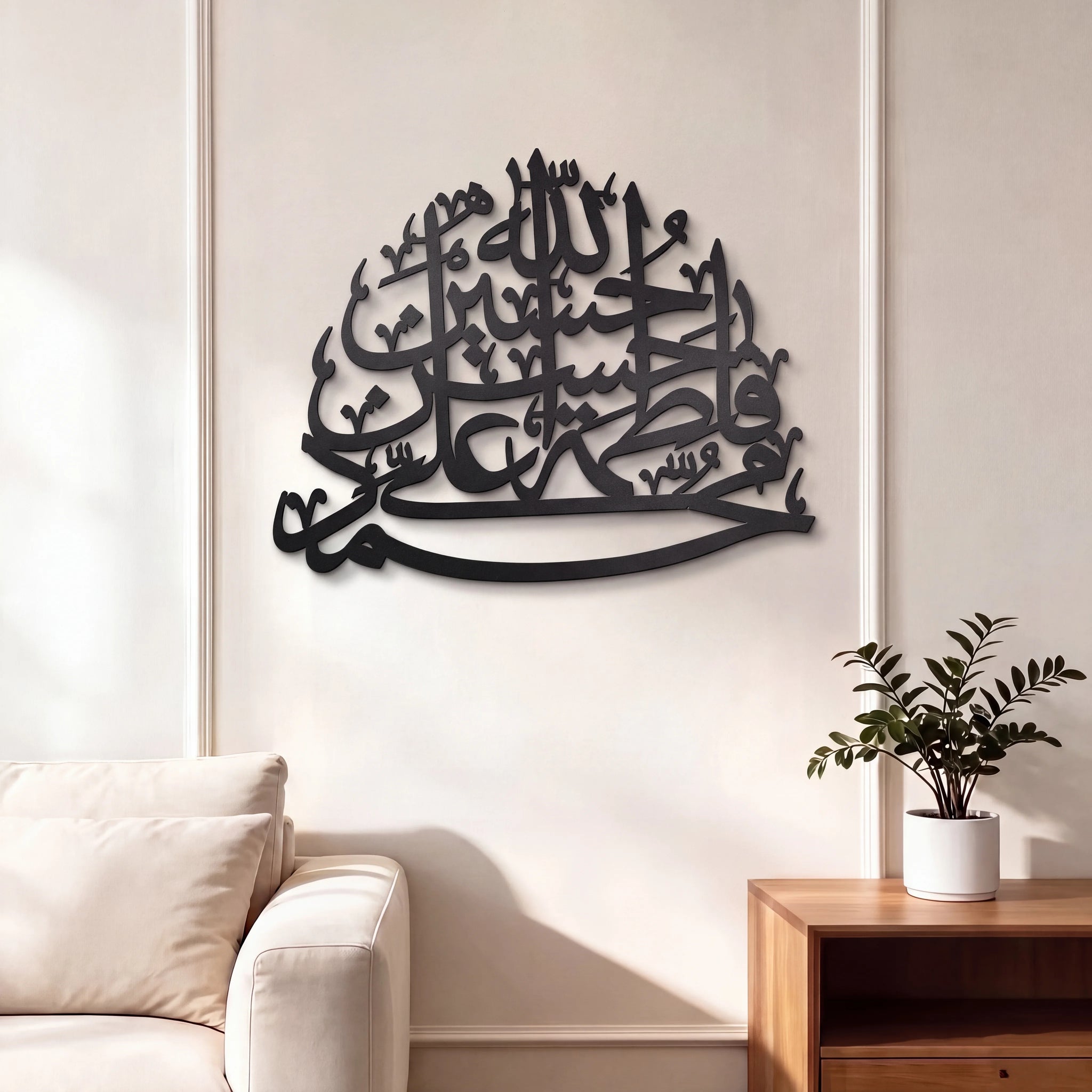 Black Panjtan Pak Metal Islamic wall art featuring Arabic calligraphy, displayed on a cream-colored wall in a modern living room setting with a sofa and wooden side table.