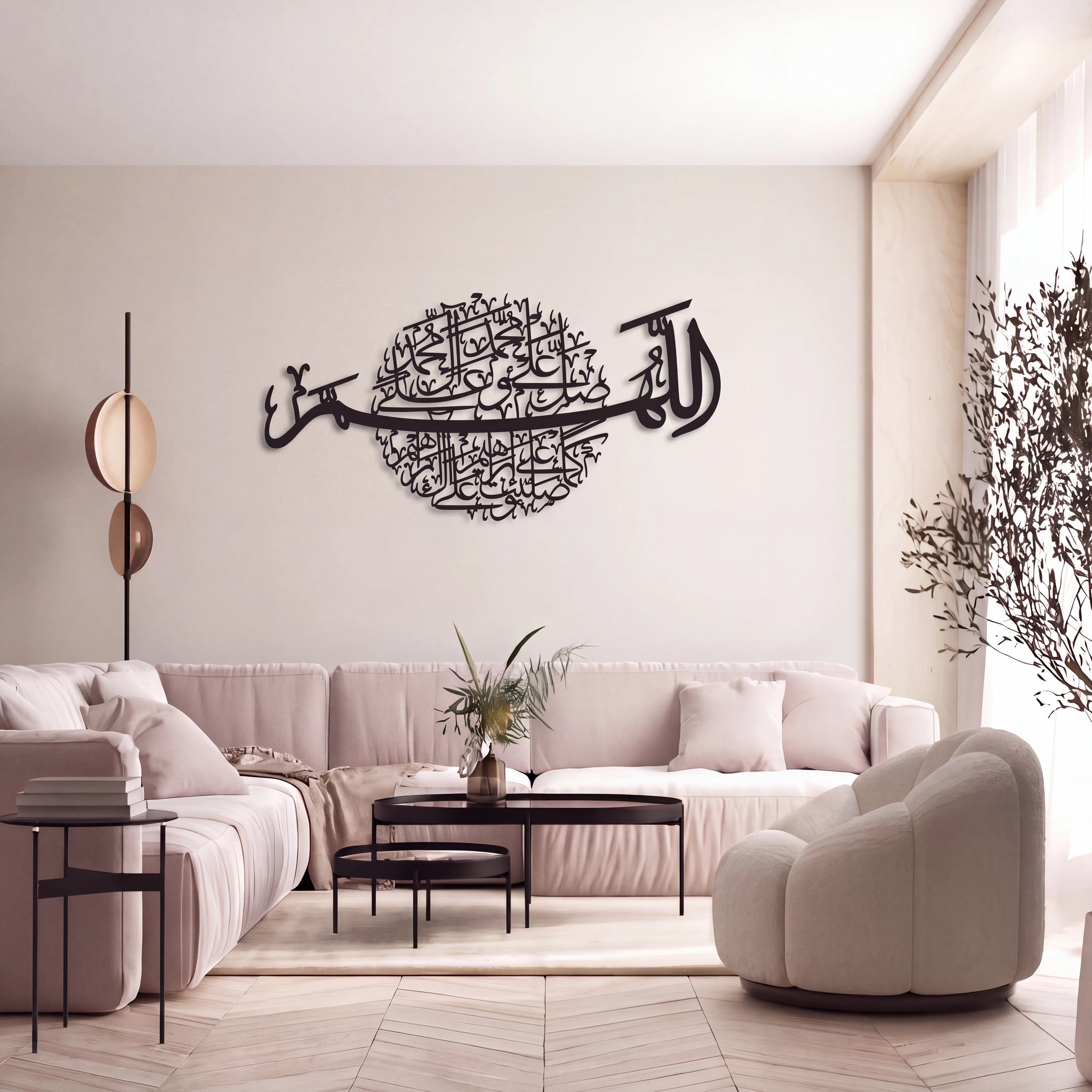 A modern living room with a Darood Shareef large black metal Islamic calligraphy wall art piece mounted on a beige wall above a light pink sectional sofa and matching armchair.