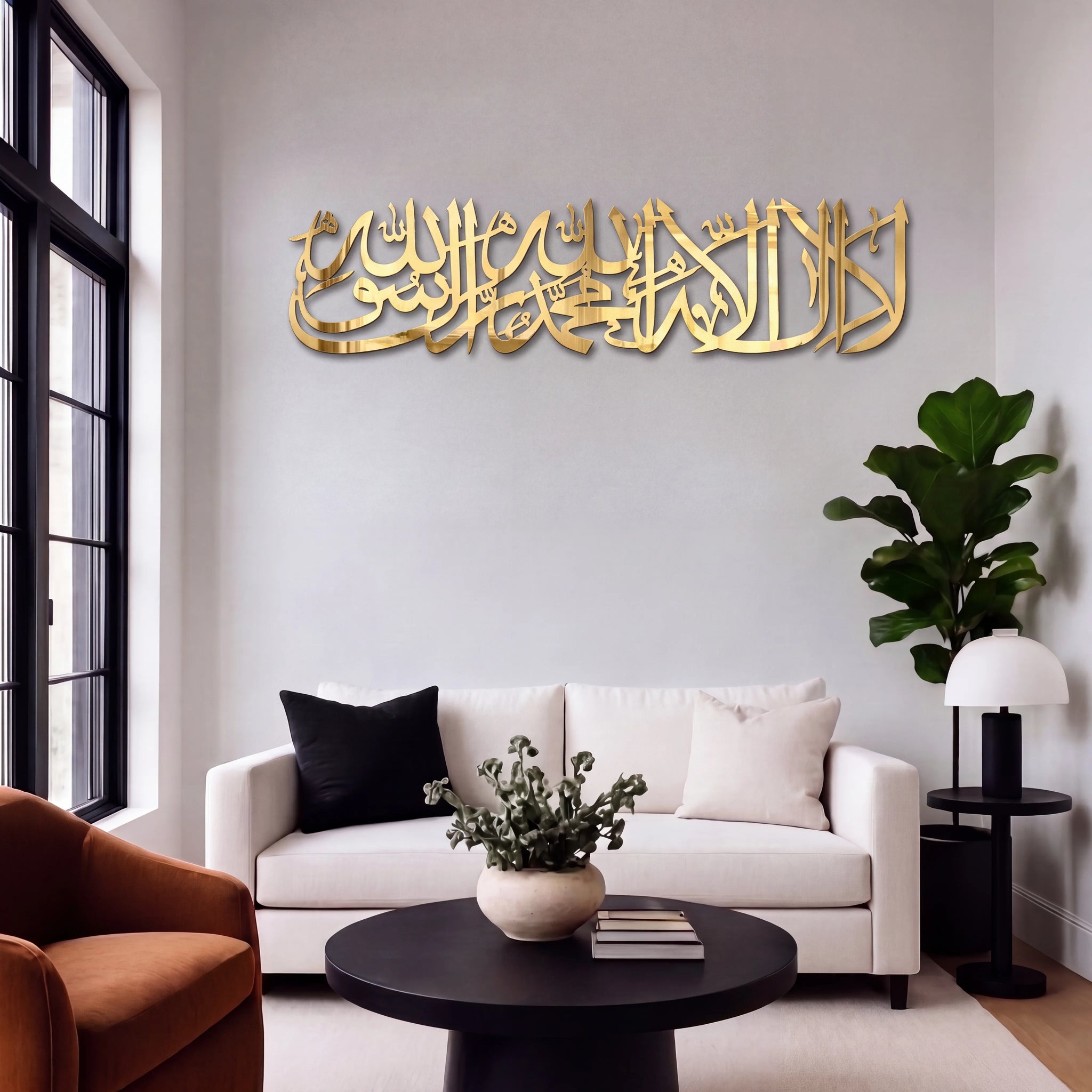 Shahada Kalima Gold Arabic calligraphy  wall art mounted on a light gray wall above a modern white sofa in a styled living room.
