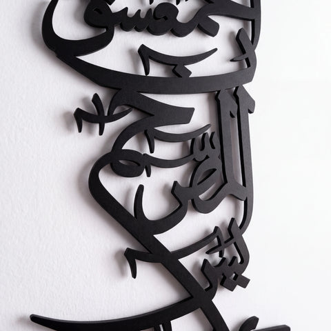 Black metal Islamic calligraphy wall art mounted on a white textured wall.