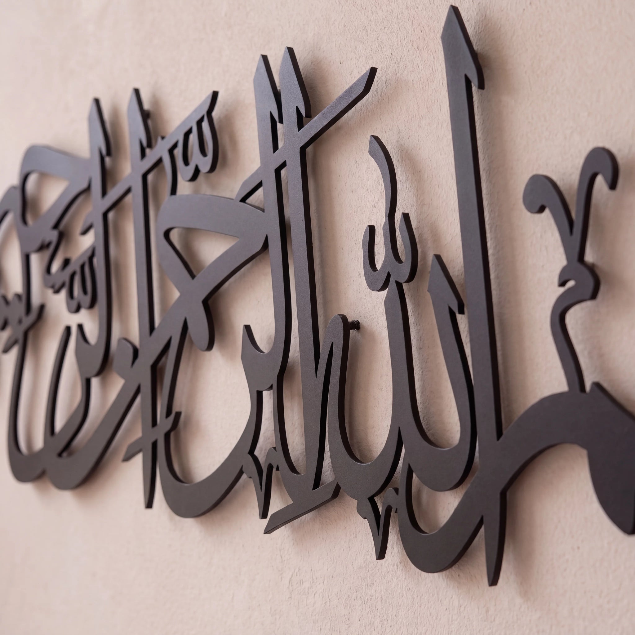 Black Bismillah metal Arabic calligraphy wall art mounted on a textured beige wall.