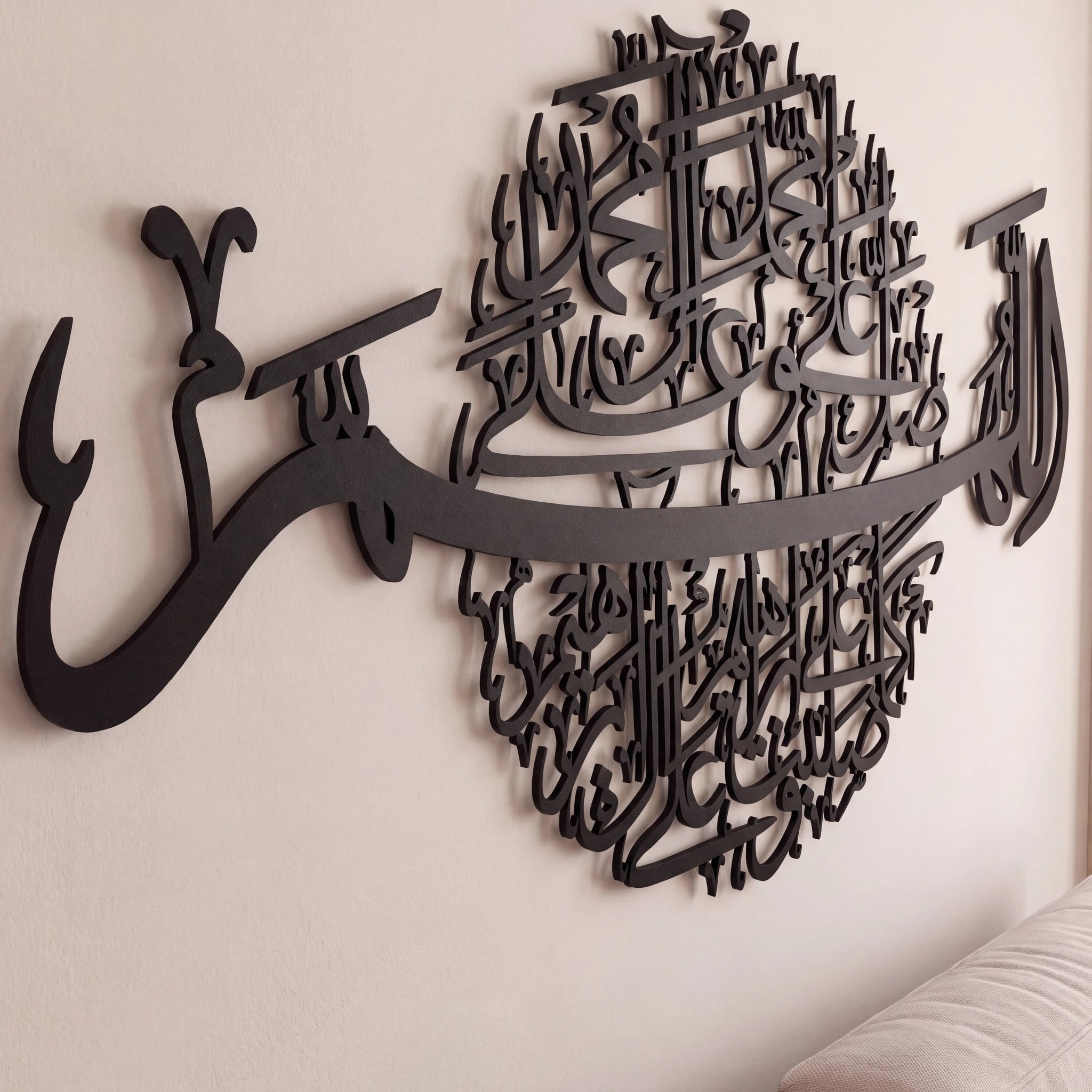 Black metal Islamic wall art featuring Arabic calligraphy spelling 'Allah' and 'Subhan Allah', mounted on a light beige wall above a white sofa.