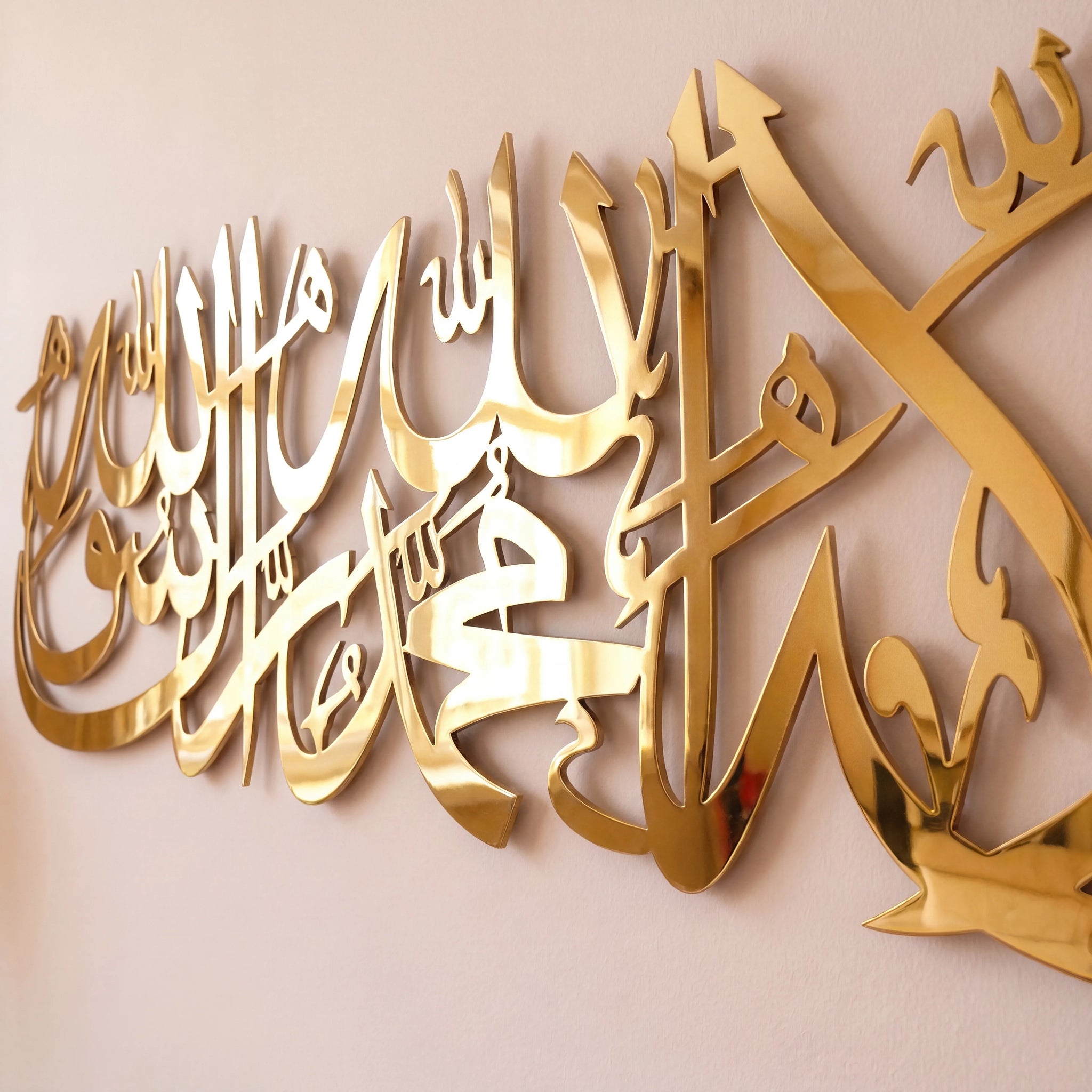 Shahada Kalima Gold metallic Arabic calligraphy wall art mounted on a light beige wall.