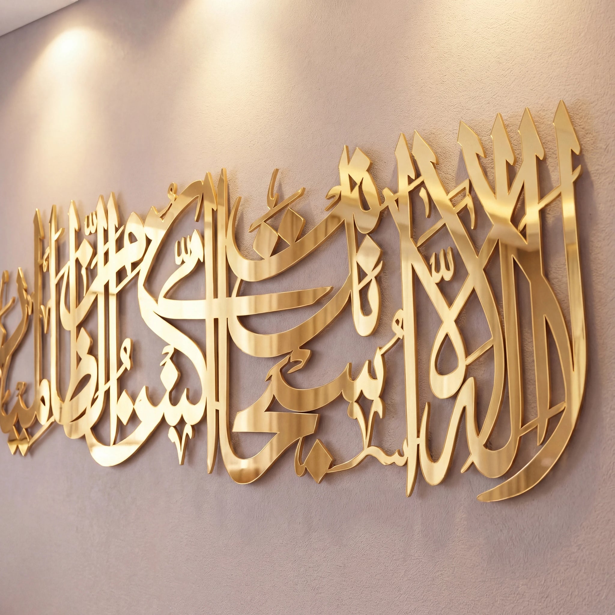Shiny Gold metallic Arabic calligraphy wall art mounted on a beige wall under warm spotlighting.