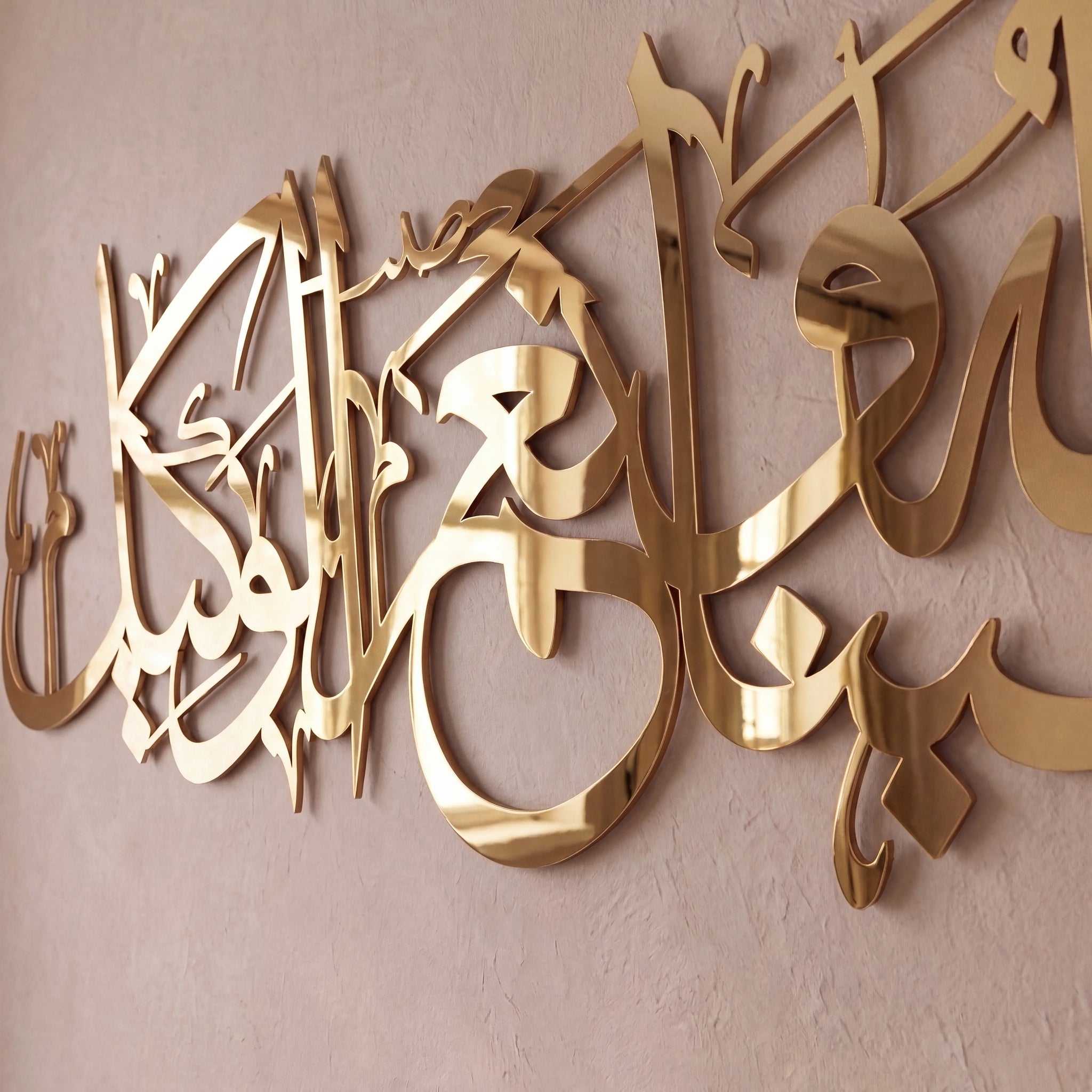 Gold metallic Arabic calligraphy wall art mounted on a textured beige wall.