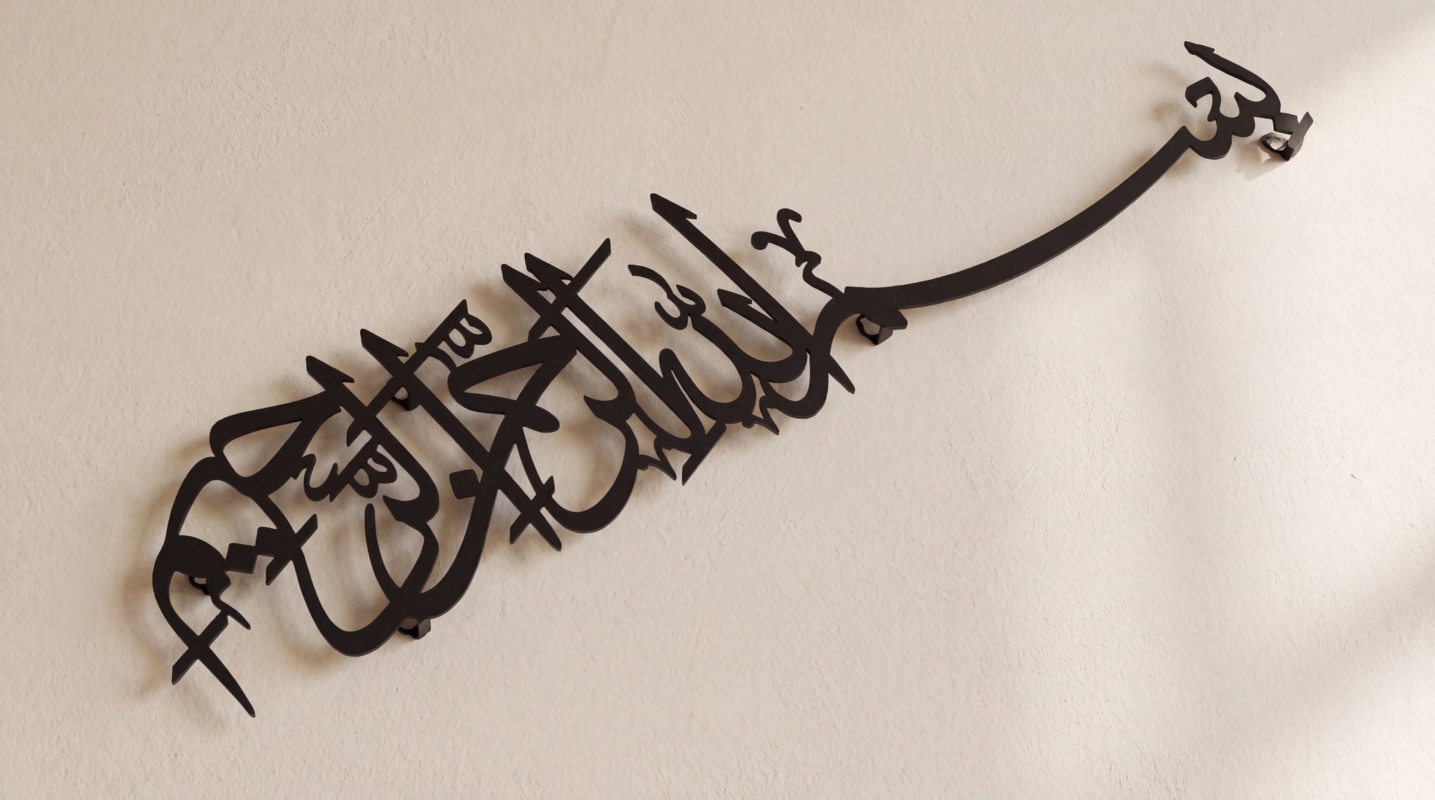 Black Bismillah metal Islamic wall art featuring Arabic calligraphy, mounted on a plain beige wall.