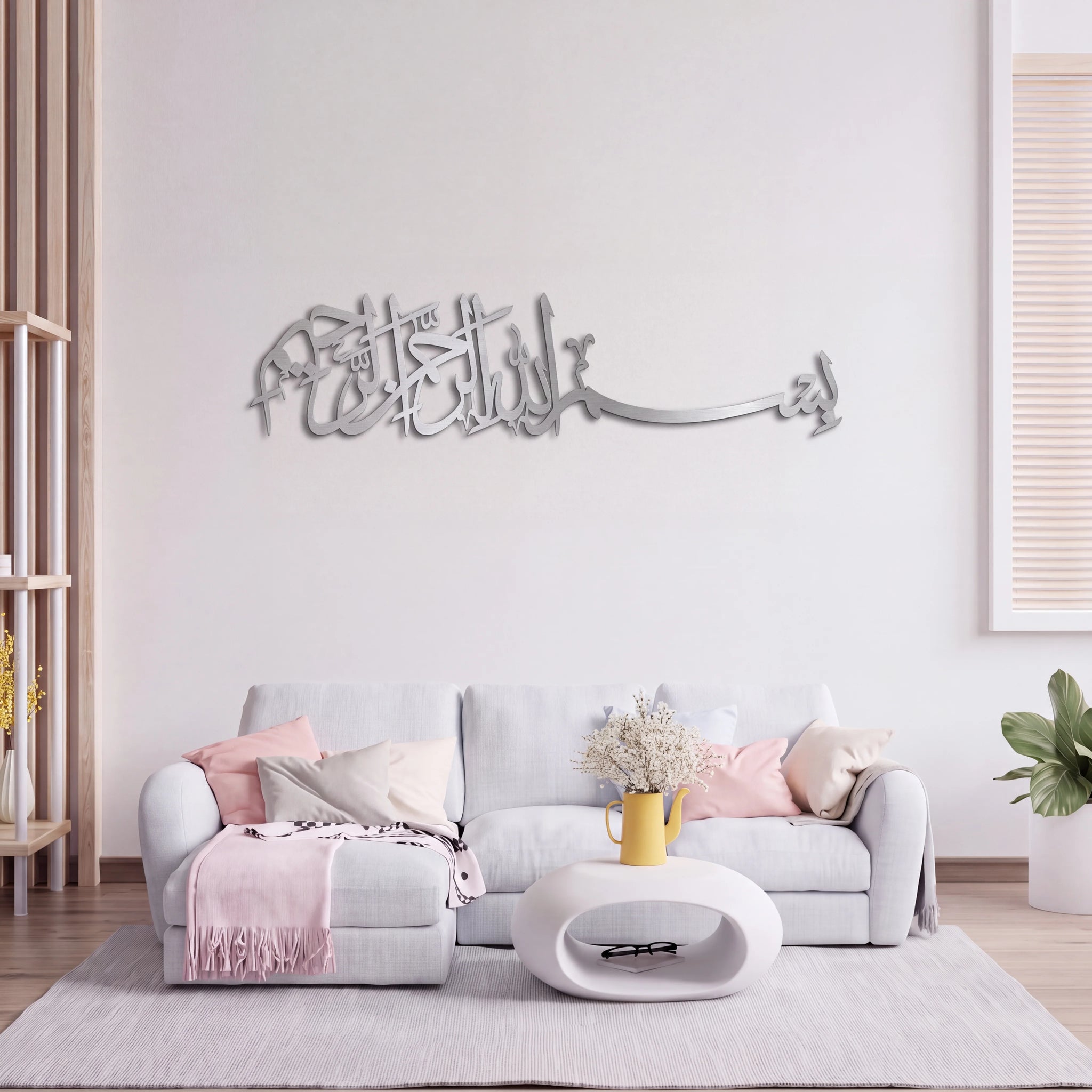Mate Silver Bismillah Arabic calligraphy wall art mounted on a white wall above a light gray sofa in a modern living room setting.
