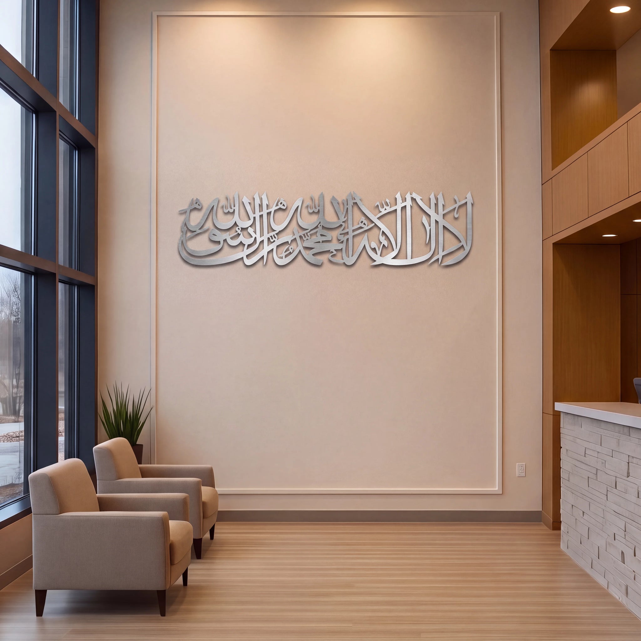 Mate Silver metallic Arabic calligraphy wall art mounted on a beige wall in a modern office lobby with wooden floors, two beige armchairs, and large windows.